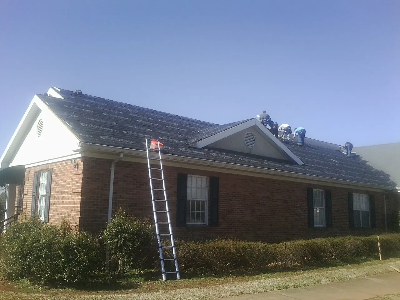 Crew tearing shingles off a brick ranch roof with a ladder set — Metal Roof Repair work by our crew in Juntura