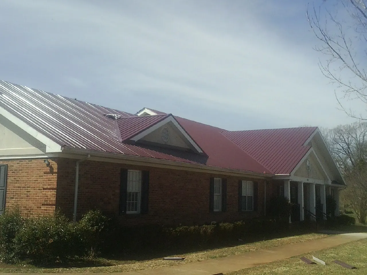 Red metal roof with gabled entries on a long brick building, from a Hail Damage Roof Repair job in Juntura