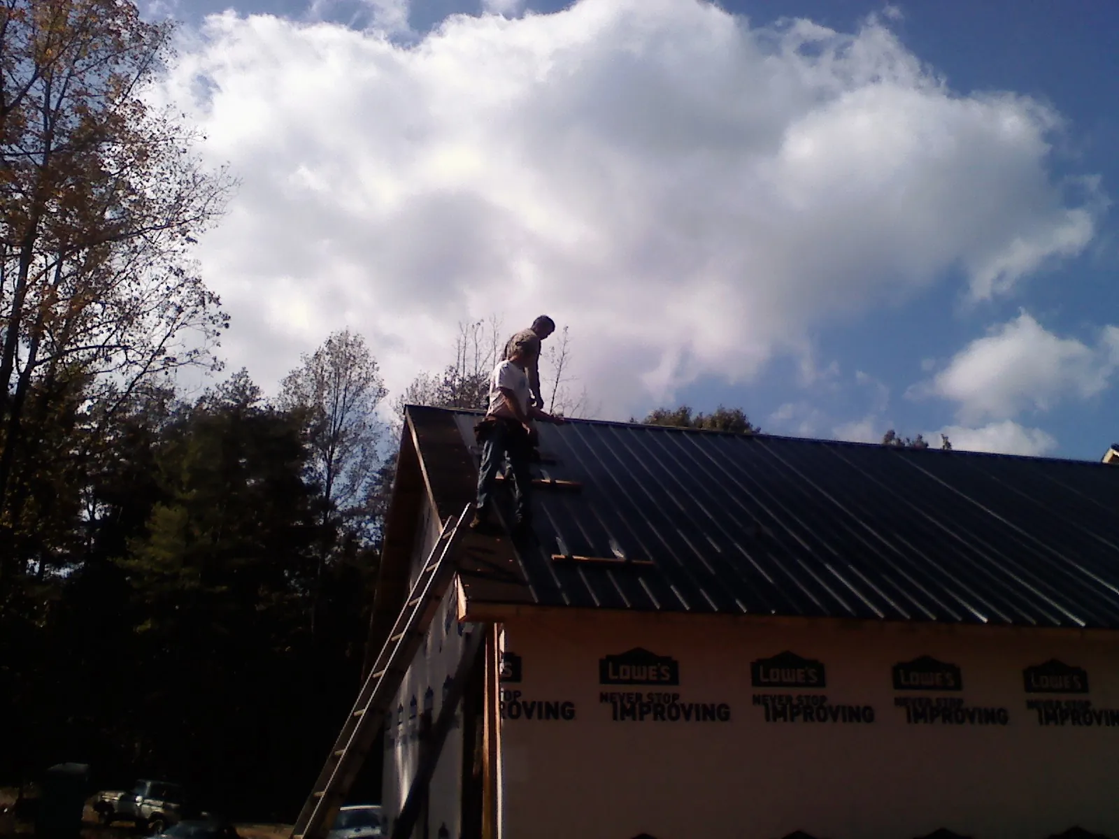 Roofer fastening dark metal panels high against a cloudy sky, from a Roof Inspection job in Juntura
