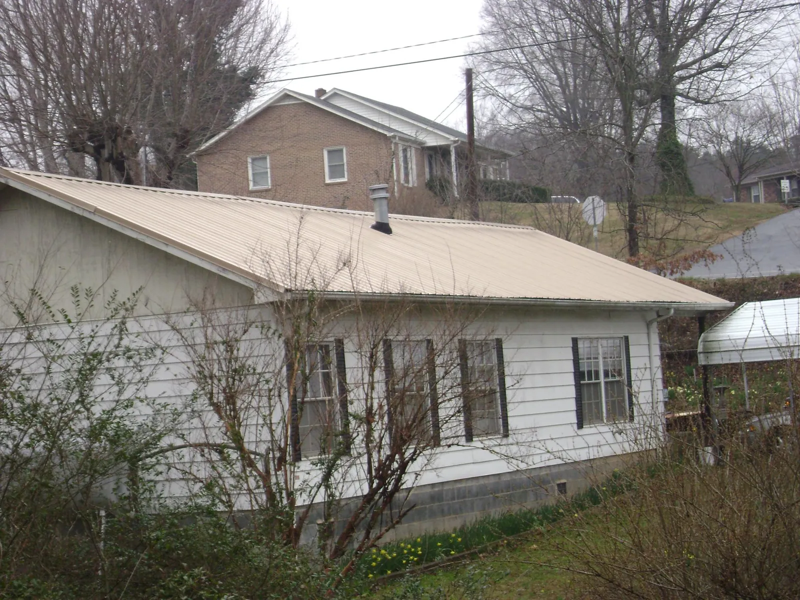 Tan metal roof on a white sided house set into a hillside — Commercial Roofing by Roofing Brothers in Juntura